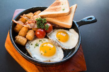 Çırpılmış yumurta tavası, kızarmış ekmek, kahverengi et, siyah arka planda domates ve ahşap tabak.,