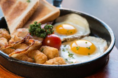 Çırpılmış yumurta tavası, kızarmış ekmek, kahverengi et, siyah arka planda domates ve ahşap tabak.,