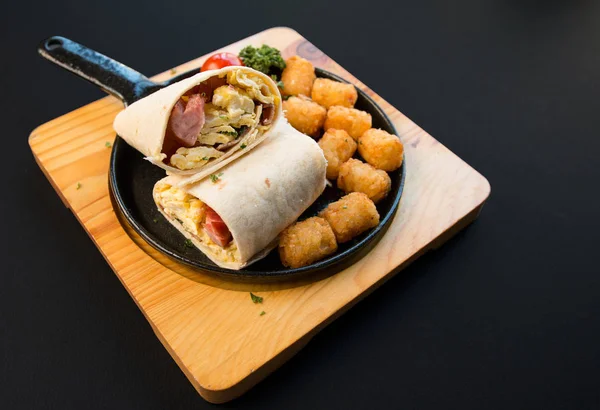 Breakfast burrito with sausage and scrambled egg and vegetable on a black background