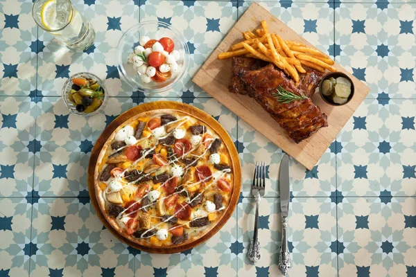 Meat,potato,vegetables topping pizza and pork rib with side dish on a table