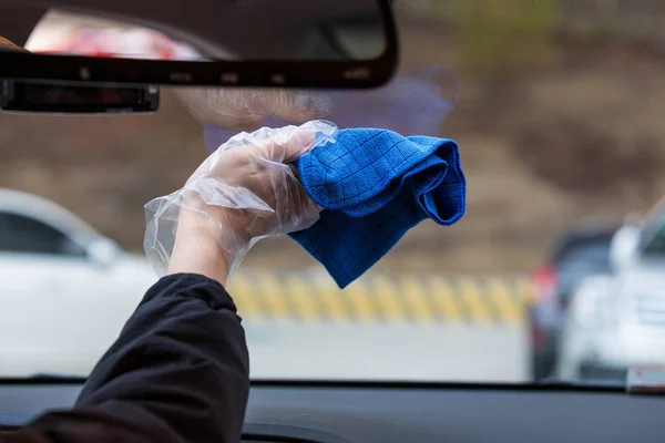 Mano sosteniendo una toalla de fibra azul para limpiar la ventana del coche. Parabrisas del coche de limpieza con tela de microfibra desde el interior . Imagen De Stock