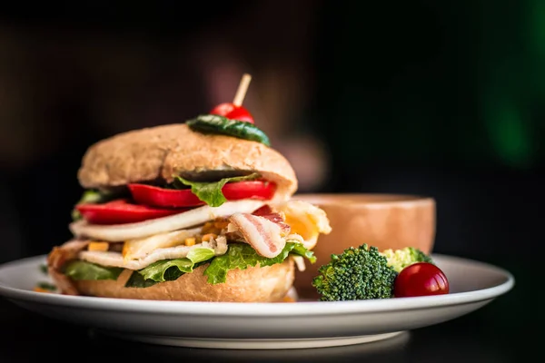 Close up image of loaded burger with cherry tomato toothpicked on the top. Vegetables bacon sandwich with black background.