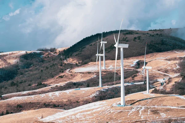 Electric Turbine Windmill on a snowy ground. Winter hill landscape with blue sky.