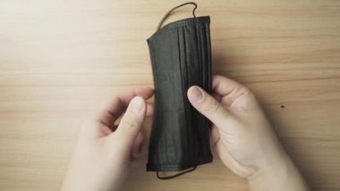 El, siyah bir yüz maskesi açıyor. Corona virüsünden korunmak için nasıl maske takılacağını gösteriyorum..