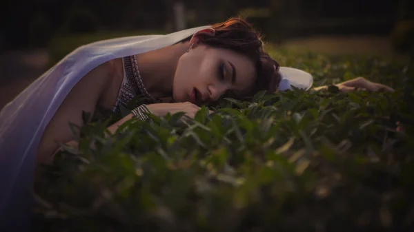 Beautiful brunette woman sleeping in a grass and flowers in the — Stock Photo, Image