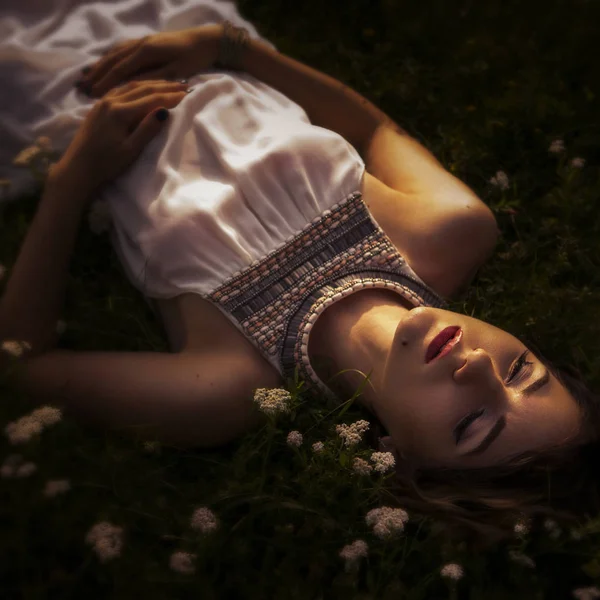 Beautiful brunette woman sleeping in a grass and flowers in the — Stock Photo, Image