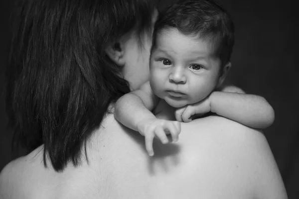 Pequeño bebé niño durmiendo acostado en los brazos de las madres. Concéntrate en un chico. Fondo negro neutro, imagen en blanco y negro. Todo en ropa blanca. Familia feliz —  Fotos de Stock