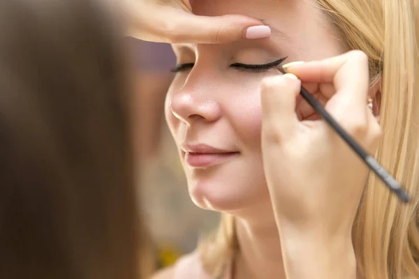 Morena maquillaje artista mujer aplicando maquillaje para un híbrido rubio —  Fotos de Stock