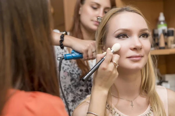 Brunette make-up artiest vrouw make up solliciteert met een blonde brid — Stockfoto