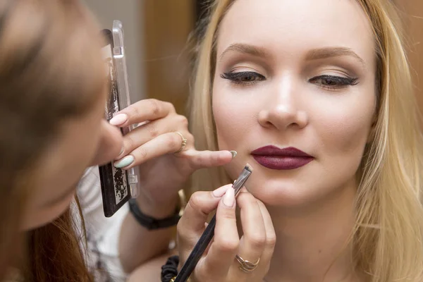 Morena maquillaje artista mujer aplicando maquillaje para un híbrido rubio —  Fotos de Stock