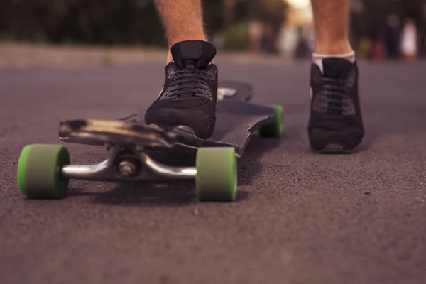Man skate voeten staande op een longboard op de weg, in park in s — Stockfoto