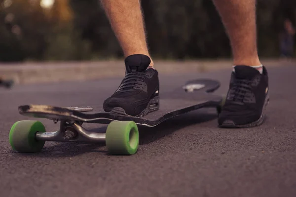 Człowieku nogi stojąc na longboard na drodze, skate park w s — Zdjęcie stockowe