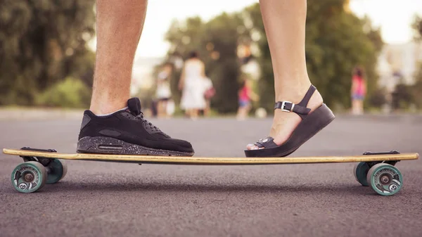 Man kissing woman, their feet standing on a longboard on the roa