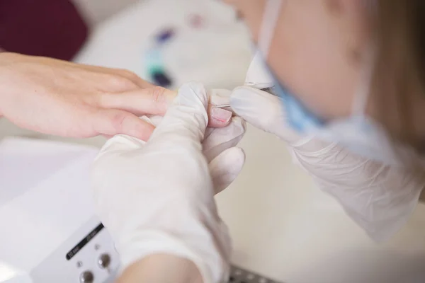 El maestro de uñas en guantes de goma hace manicura usando la máquina de manicura —  Fotos de Stock