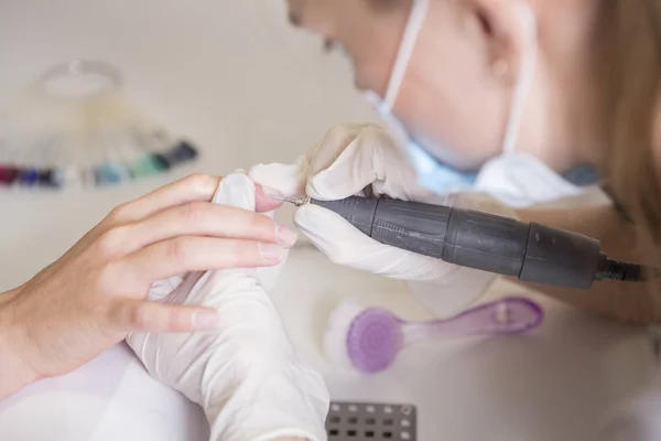 Nail master in rubber gloves make manicure using manicure machin