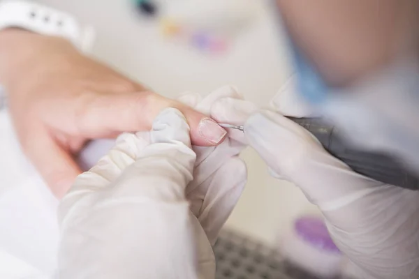 El maestro de uñas en guantes de goma hace manicura usando la máquina de manicura —  Fotos de Stock