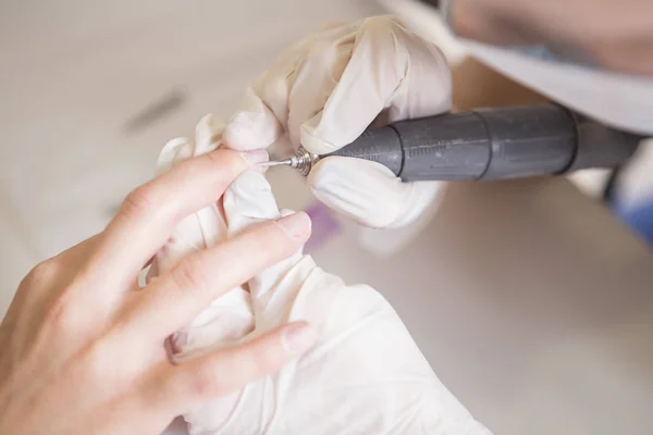 El maestro de uñas en guantes de goma hace manicura usando la máquina de manicura —  Fotos de Stock