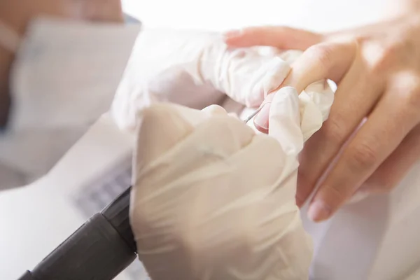 El maestro de uñas en guantes de goma hace manicura usando la máquina de manicura —  Fotos de Stock