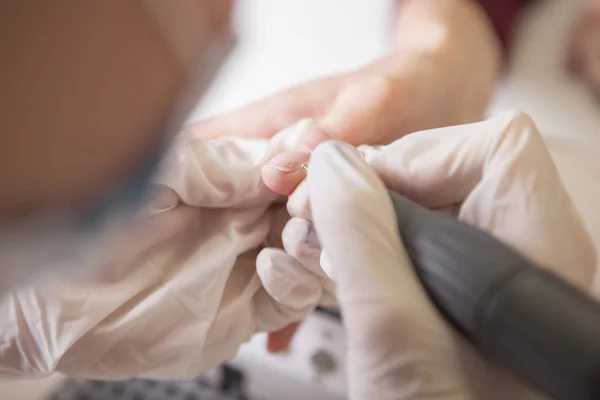 El maestro de uñas en guantes de goma hace manicura usando la máquina de manicura —  Fotos de Stock