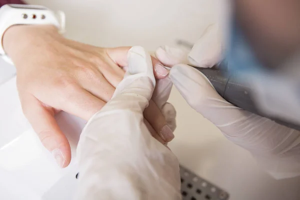 El maestro de uñas en guantes de goma hace manicura usando la máquina de manicura —  Fotos de Stock