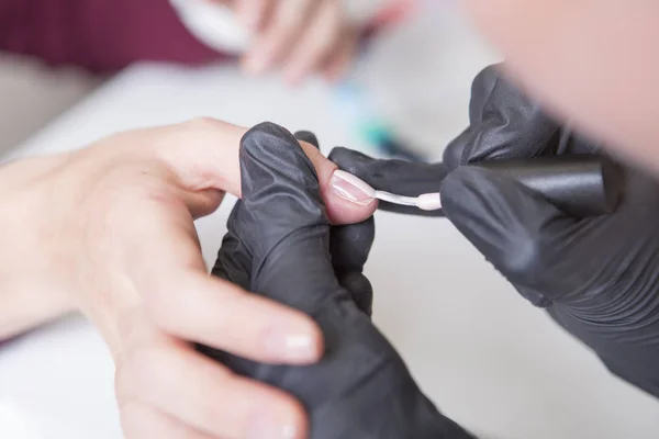 Nail master in rubber gloves apply gel polish shellac on a woman