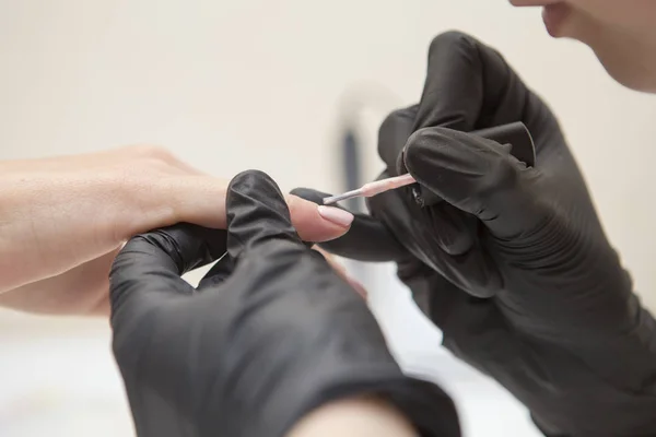 Maestro de uñas en guantes de goma aplicar gel laca laca en una mujer —  Fotos de Stock