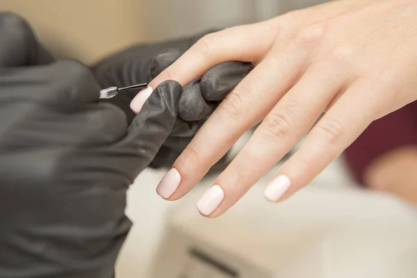 Nail master in rubber gloves apply gel polish shellac on a woman — Stock Photo, Image