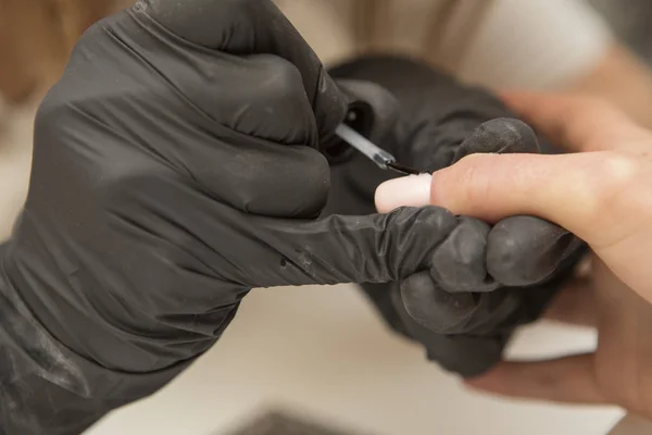 Maestro de uñas en guantes de goma aplicar gel laca laca en una mujer —  Fotos de Stock