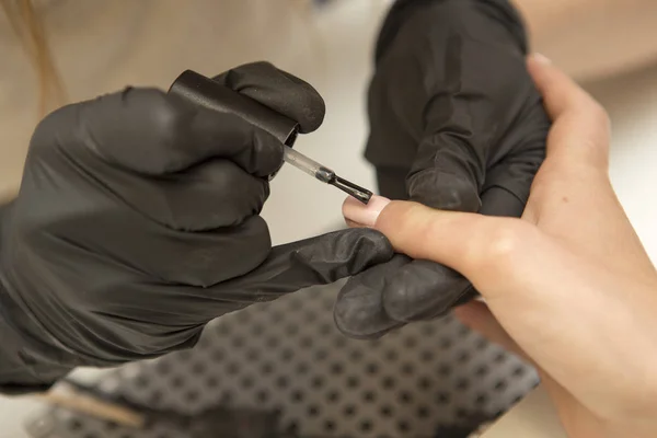 Nail master in rubber gloves apply gel polish shellac on a woman