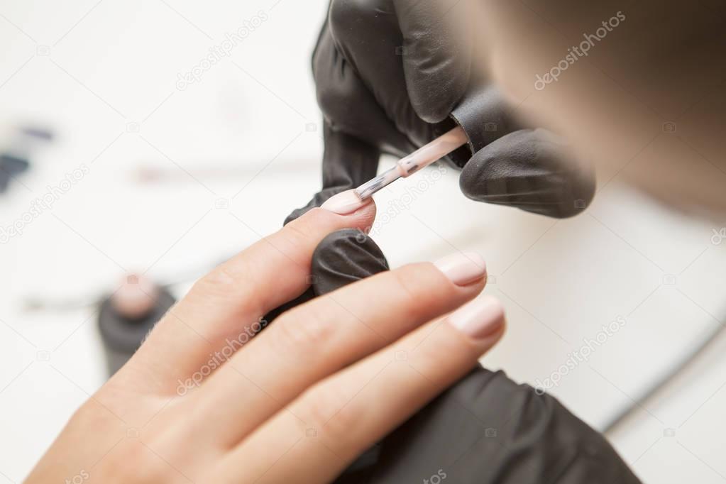 Nail master in rubber gloves apply gel polish shellac on a woman