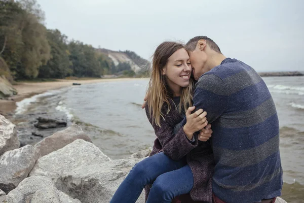 Happy thoughtful couple sitting on a rock beach near sea hugging — Stock Photo, Image