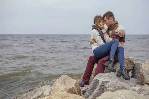 Happy thoughtful couple sitting on a rock beach near sea hugging — Stock Photo, Image