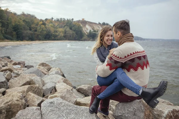 Glada omtänksamma paret sitter på en rock strand nära havet-kramas — Stockfoto