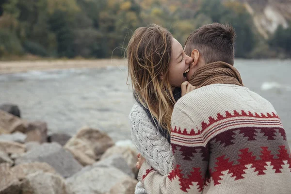 Glückliches nachdenkliches Paar sitzt auf einem Felsstrand in der Nähe des Meeres und umarmt sich — Stockfoto
