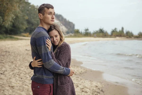 Feliz casal pensativo em pé em uma praia de rocha perto do abraço do mar — Fotografia de Stock