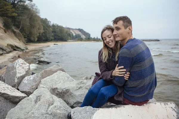 Feliz casal pensativo sentado em uma praia de rocha perto do mar abraçando — Fotografia de Stock