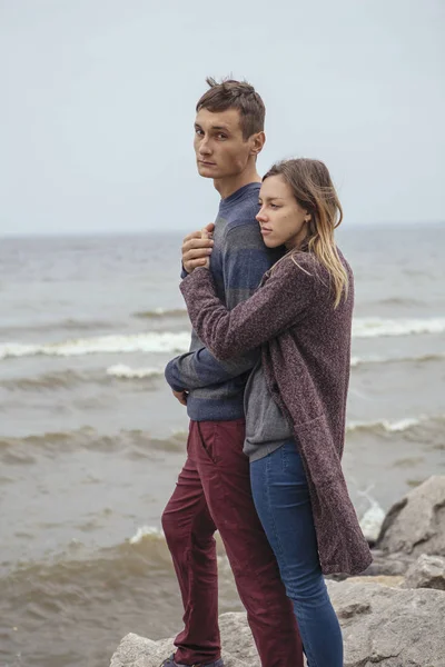 Happy thoughtful couple standing on a rock beach near sea huggin — Stock Photo, Image