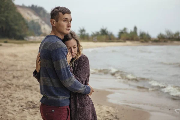 Felice coppia premurosa in piedi su una spiaggia rocciosa vicino abbraccio mare — Foto Stock