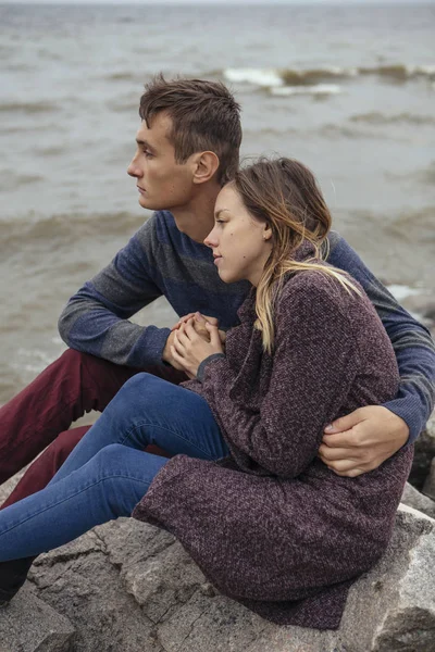Ευτυχισμένος στοχαστικό ζευγάρι κάθεται σε έναν βράχο στην παραλία κοντά στη θάλασσα αγκαλιάζει — Φωτογραφία Αρχείου