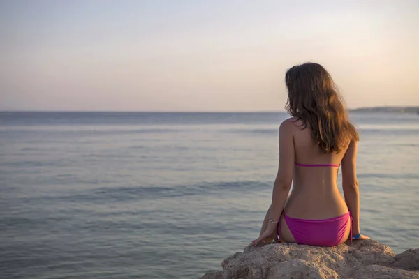 Jonge sexy brunette vrouw met lang haar, zittend op een rots in pi — Stockfoto