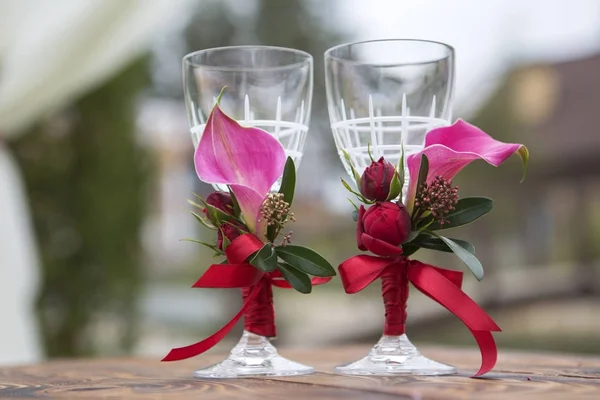Set of wedding glassess with wine color flowers and ribbon on a wooden surface (table). Outdoors. Copy space