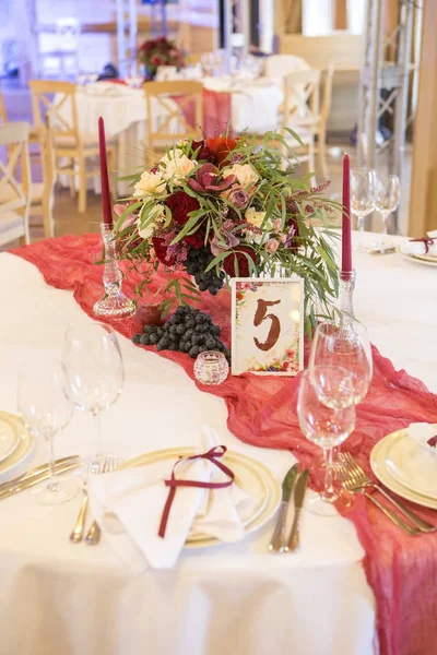 Set of wine flowers on a wedding table surrounded by plates, tab
