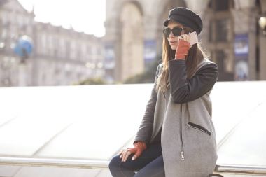 Mutlu bir telefonda konuşurken gülümseyen esmer genç beyaz kadın rahat ceket (ceket), kot pantolon ve Avrupa şehir sokakları, yürüyüş güneş gözlüğü. Yaşam tarzı portre kapalı. Kopya alanı