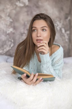 Kitap okuma bir yatak üzerinde oturan genç güzel beyaz kadın. O gündelik kıyafeti giymiş: Mavi kazak ve kot pantolon. Uzun kahverengi saçlı, ufak bir gülümseme, düşünceli arıyorum