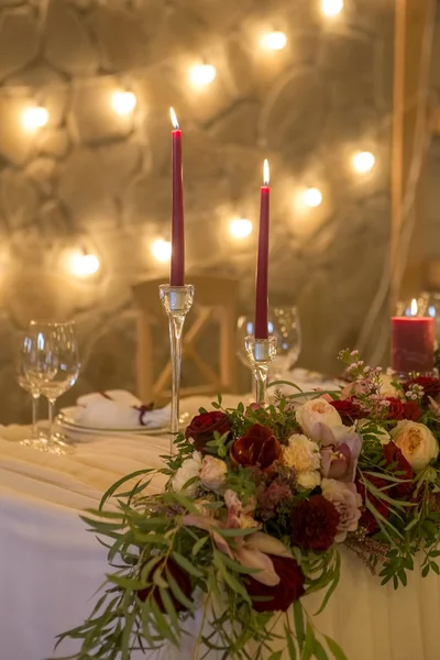 Set of wine color candles on a wedding table surrounded by light garland and flowers. Interior. Copy space