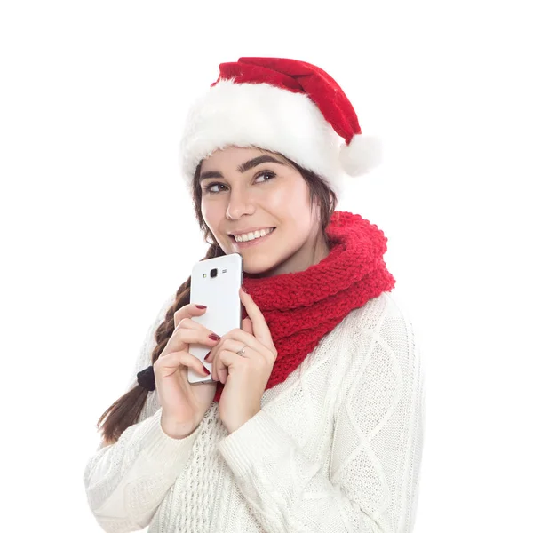 可爱的十几岁的女孩 黑色长发站在白色的毛衣 红色的围巾和圣诞老人的帽子 在她的手中 在她的手 打字短信白背景 情感生活肖像 — 图库照片