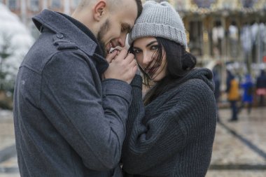Muhteşem güzel beyaz bir kadın kış Avrupa kenti bir yolda bir adamla. Çift sıradan gri kıyafet ve birbirlerine sarılma giymek. Soğuk hava, bir arka plan üzerinde Noel ışıkları