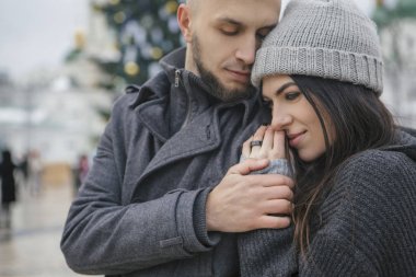 Muhteşem güzel beyaz bir kadın kış Avrupa kenti bir yolda bir adamla. Çift sıradan gri kıyafet ve birbirlerine sarılma giymek. Soğuk hava, bir arka plan üzerinde Noel ışıkları