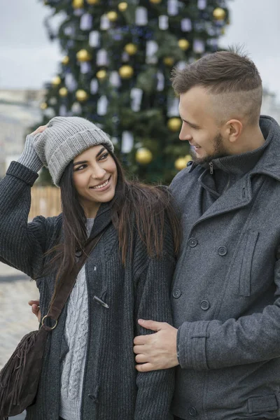 美丽的白种女人与一个男人在欧洲城市的冬天散步 夫妇穿着休闲灰色的衣服和拥抱对方 寒冷的天气 背景下的圣诞灯 — 图库照片