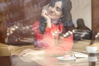 Şirin esmer bir mesafe (serbest) çalışma, kafede oturup, kahve içme ve yemek macaron boyutu kadın artı. O kırmızı kazak giyen dinlemek müzik ve ona telefon iletileri yazma